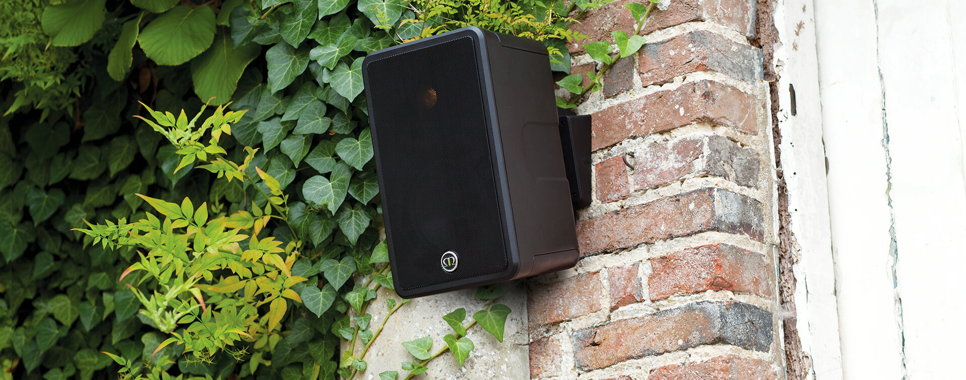 Black Monitor Audio Climate 50 outdoor speaker mounted on brick wall