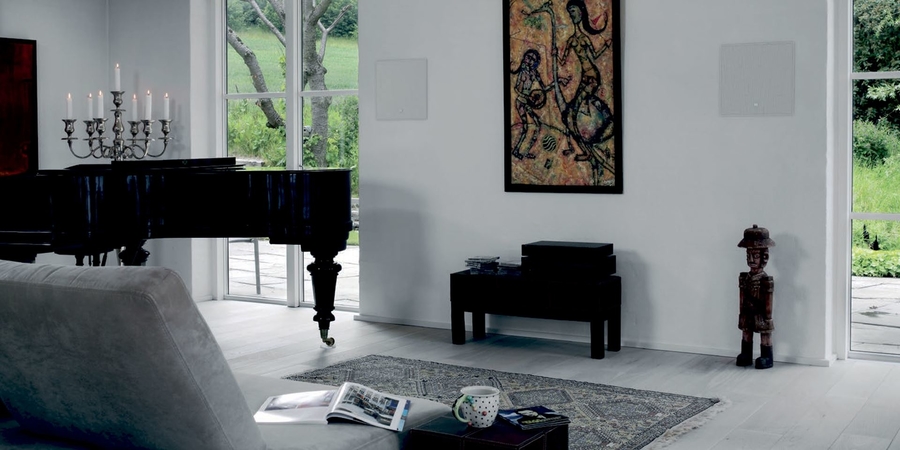 Two white grille speakers in wall in a modern living space next to a black piano